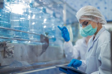 Bilim adamı, endüstriyel fabrikanın makine taşıma hattındaki su şişelerinin kalitesini kontrol ediyor. İçki üretim hattında veri kaydeden kadın işçi..