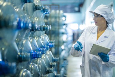 Fabrika işçisi endüstriyel fabrikadaki depoda su şişelerini kontrol ediyor. İçki üretim hattında veri kaydeden kadın işçi..