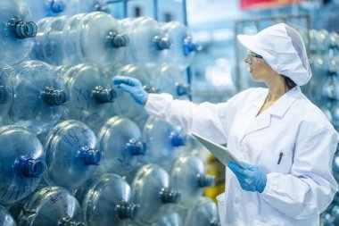 Fabrika işçisi endüstriyel fabrikadaki depoda su şişelerini kontrol ediyor. İçki üretim hattında veri kaydeden kadın işçi..
