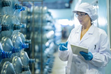 Fabrika işçisi endüstriyel fabrikadaki depoda su şişelerini kontrol ediyor. İçki üretim hattında veri kaydeden kadın işçi..
