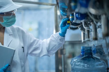 Bilim adamı, endüstriyel fabrikanın makine taşıma hattındaki su şişelerinin kalitesini kontrol ediyor. İçki üretim hattında veri kaydeden kadın işçi..