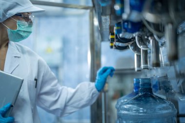 Bilim adamı, endüstriyel fabrikanın makine taşıma hattındaki su şişelerinin kalitesini kontrol ediyor. İçki üretim hattında veri kaydeden kadın işçi..