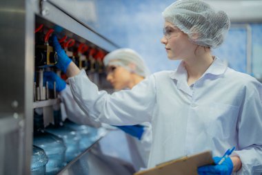 Bilim adamı, endüstriyel fabrikanın makine taşıma hattındaki su şişelerinin kalitesini kontrol ediyor. İçki üretim hattında veri kaydeden kadın işçi..