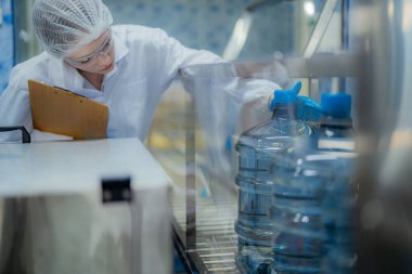 Bilim adamı, endüstriyel fabrikanın makine taşıma hattındaki su şişelerinin kalitesini kontrol ediyor. İçki üretim hattında veri kaydeden kadın işçi..