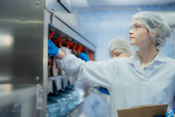 科学者の労働者は工業工場の機械コンベアラインの水ボトルの品質をチェックしています 飲料製造ラインでデータを記録する女性労働者 — ストック写真