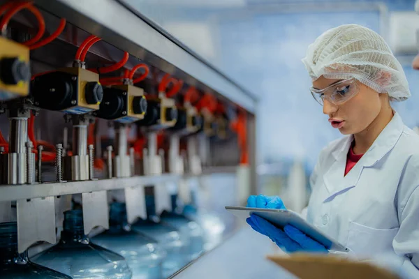 科学者の労働者は工業工場の機械コンベアラインの水ボトルの品質をチェックしています 飲料製造ラインでデータを記録する女性労働者 — ストック写真