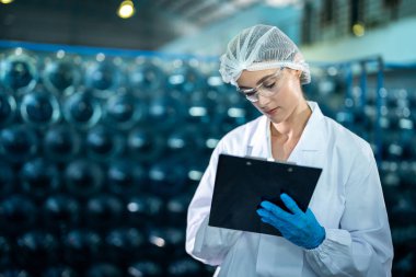 Fabrika işçisi endüstriyel fabrikadaki depoda su şişelerini kontrol ediyor. İçki üretim hattında veri kaydeden kadın işçi..