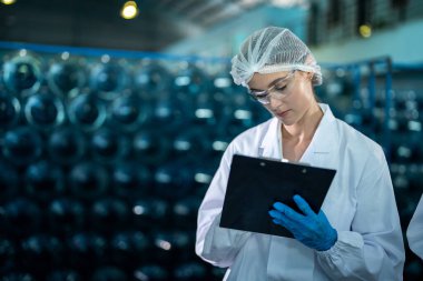 Fabrika işçisi endüstriyel fabrikadaki depoda su şişelerini kontrol ediyor. İçki üretim hattında veri kaydeden kadın işçi..