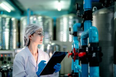 Endüstriyel fabrikadaki ters osmoz makinesinin kalitesini kontrol eden bilim adamı. Geri dönüşümlü taşınabilir fabrika için ölçü basıncıyla kontrol panelinde veri kaydeden kadın işçi.