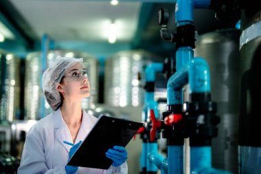 Endüstriyel fabrikadaki ters osmoz makinesinin kalitesini kontrol eden bilim adamı. Geri dönüşümlü taşınabilir fabrika için ölçü basıncıyla kontrol panelinde veri kaydeden kadın işçi.