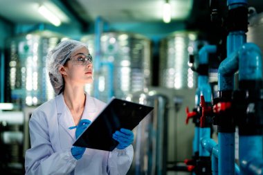 Endüstriyel fabrikadaki ters osmoz makinesinin kalitesini kontrol eden bilim adamı. Geri dönüşümlü taşınabilir fabrika için ölçü basıncıyla kontrol panelinde veri kaydeden kadın işçi.