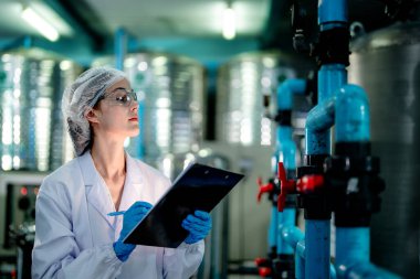 Endüstriyel fabrikadaki ters osmoz makinesinin kalitesini kontrol eden bilim adamı. Geri dönüşümlü taşınabilir fabrika için ölçü basıncıyla kontrol panelinde veri kaydeden kadın işçi.