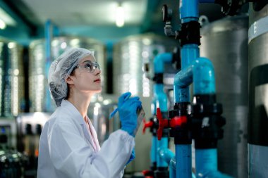 Endüstriyel fabrikadaki ters osmoz makinesinin kalitesini kontrol eden bilim adamı. Geri dönüşümlü taşınabilir fabrika için ölçü basıncıyla kontrol panelinde veri kaydeden kadın işçi.