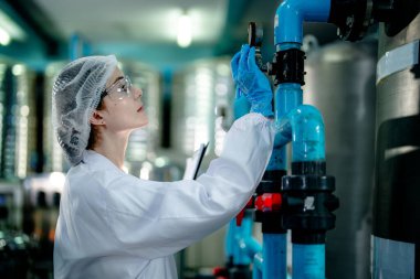 Endüstriyel fabrikadaki ters osmoz makinesinin kalitesini kontrol eden bilim adamı. Geri dönüşümlü taşınabilir fabrika için ölçü basıncıyla kontrol panelinde veri kaydeden kadın işçi.