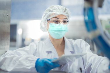 Kadın fabrika işçileri endüstriyel fabrikadaki makine sistemlerini kontrol ediyorlar. Kadınlar içecek ve gıda üretimi için temiz odalarda çalışıyorlar