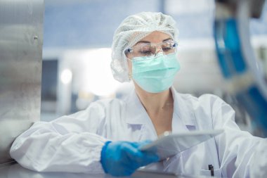 Kadın fabrika işçileri endüstriyel fabrikadaki makine sistemlerini kontrol ediyorlar. Kadınlar içecek ve gıda üretimi için temiz odalarda çalışıyorlar