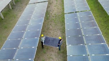 Güneş panelleri tutan ve güneş çiftliğinde yürüyen işçilerin en iyi görüntüsü. Mühendisler güneş pili panelinin yapımını denetliyor. İHA uçuşu güneş panelleri üzerinde uçar yenilenebilir yeşil enerji alanı üzerinde.