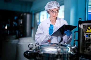 Fabrika işçisi endüstriyel fabrikadaki depoda su şişelerini kontrol ediyor. İçki üretim hattında veri kaydeden kadın işçi..