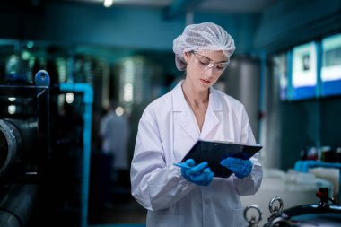 Fabrika işçisi endüstriyel fabrikadaki depoda su şişelerini kontrol ediyor. İçki üretim hattında veri kaydeden kadın işçi..