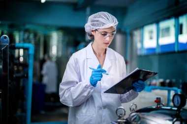 Fabrika işçisi endüstriyel fabrikadaki depoda su şişelerini kontrol ediyor. İçki üretim hattında veri kaydeden kadın işçi..