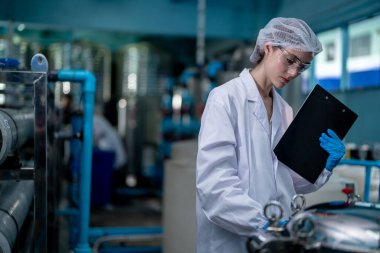 Fabrika işçisi endüstriyel fabrikadaki depoda su şişelerini kontrol ediyor. İçki üretim hattında veri kaydeden kadın işçi..
