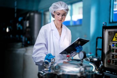 Fabrika işçisi endüstriyel fabrikadaki depoda su şişelerini kontrol ediyor. İçki üretim hattında veri kaydeden kadın işçi..