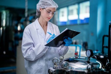 Fabrika işçisi endüstriyel fabrikadaki depoda su şişelerini kontrol ediyor. İçki üretim hattında veri kaydeden kadın işçi..