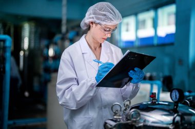 Fabrika işçisi endüstriyel fabrikadaki depoda su şişelerini kontrol ediyor. İçki üretim hattında veri kaydeden kadın işçi..