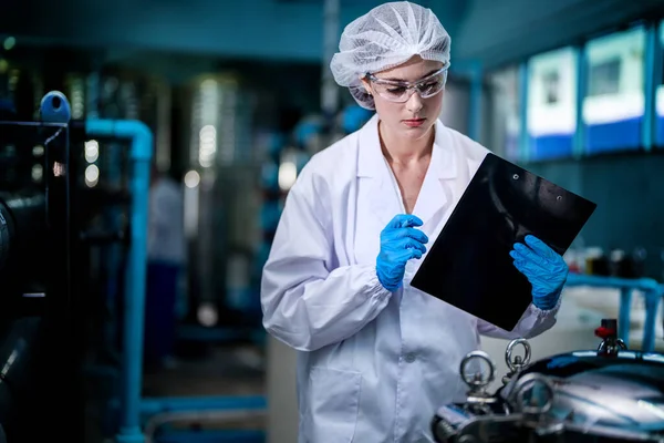 工場で倉庫内のウォーターボトルをチェックする工場労働者 飲料製造ラインでデータを記録する女性労働者 — ストック写真