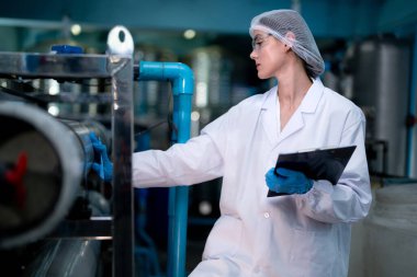 Fabrika çalışanı endüstriyel fabrikadaki depoda su şişelerini kontrol ediyor. İçki üretim hattında veri kaydeden kadın işçi..