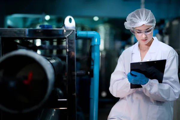 工場の女性労働者は工業工場の倉庫の水ボトルを点検しました 飲料製造ライン生産における女性労働者の記録データ — ストック写真