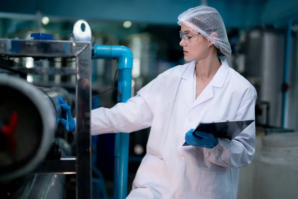 工場の女性労働者は工業工場の倉庫の水ボトルを点検しました 飲料製造ライン生産における女性労働者の記録データ — ストック写真