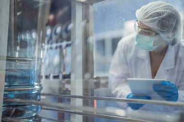 Bilim adamı, endüstriyel fabrikanın makine taşıma hattındaki su şişelerinin kalitesini kontrol ediyor. İçki üretim hattında veri kaydeden kadın işçi..