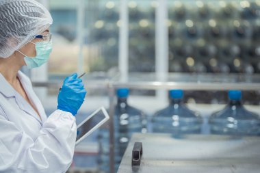 Kadın fabrika işçileri endüstriyel fabrikadaki makine sistemlerini kontrol ediyorlar. Kadınlar içecek ve gıda üretimi için temiz odalarda çalışıyorlar