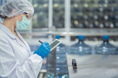 Bilim adamı, endüstriyel fabrikanın makine taşıma hattındaki su şişelerinin kalitesini kontrol ediyor. İçki üretim hattında veri kaydeden kadın işçi..