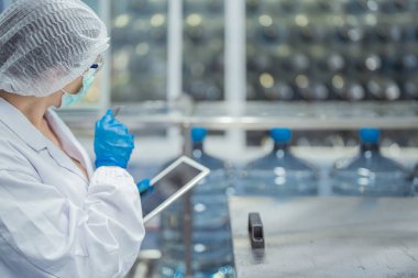 Kadın fabrika işçileri endüstriyel fabrikadaki makine sistemlerini kontrol ediyorlar. Kadınlar içecek ve gıda üretimi için temiz odalarda çalışıyorlar