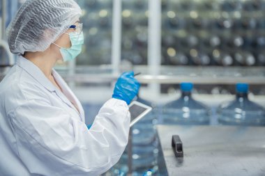 Kadın fabrika işçileri endüstriyel fabrikadaki makine sistemlerini kontrol ediyorlar. Kadınlar içecek ve gıda üretimi için temiz odalarda çalışıyorlar