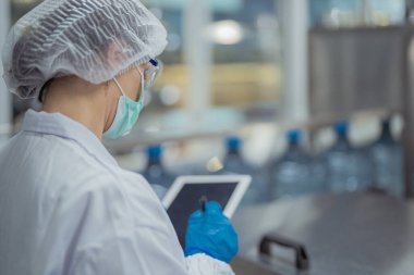 Bilim adamı, endüstriyel fabrikanın makine taşıma hattındaki su şişelerinin kalitesini kontrol ediyor. İçki üretim hattında veri kaydeden kadın işçi..