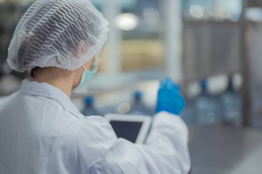 Bilim adamı, endüstriyel fabrikanın makine taşıma hattındaki su şişelerinin kalitesini kontrol ediyor. İçki üretim hattında veri kaydeden kadın işçi..