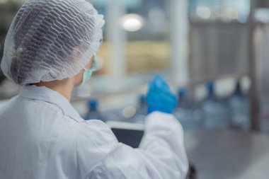 Bilim adamı, endüstriyel fabrikanın makine taşıma hattındaki su şişelerinin kalitesini kontrol ediyor. İçki üretim hattında veri kaydeden kadın işçi..