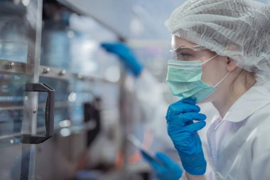 Bilim adamı, endüstriyel fabrikanın makine taşıma hattındaki su şişelerinin kalitesini kontrol ediyor. İçki üretim hattında veri kaydeden kadın işçi..