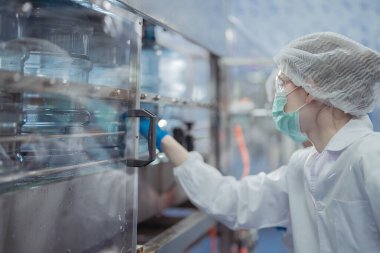 Kadın fabrika işçileri endüstriyel fabrikadaki makine sistemlerini kontrol ediyorlar. Kadınlar içecek ve gıda üretimi için temiz odalarda çalışıyorlar