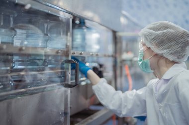 Bilim adamı, endüstriyel fabrikanın makine taşıma hattındaki su şişelerinin kalitesini kontrol ediyor. İçki üretim hattında veri kaydeden kadın işçi..