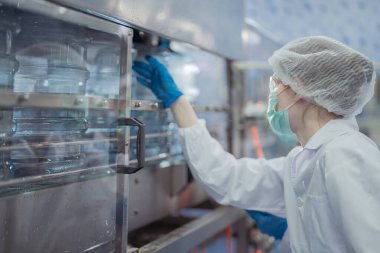 Bilim adamı, endüstriyel fabrikanın makine taşıma hattındaki su şişelerinin kalitesini kontrol ediyor. İçki üretim hattında veri kaydeden kadın işçi..