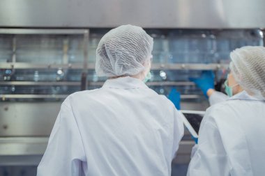 Bilim adamı, endüstriyel fabrikanın makine taşıma hattındaki su şişelerinin kalitesini kontrol ediyor. İçki üretim hattında veri kaydeden kadın işçi..