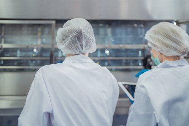 Bilim adamı, endüstriyel fabrikanın makine taşıma hattındaki su şişelerinin kalitesini kontrol ediyor. İçki üretim hattında veri kaydeden kadın işçi..