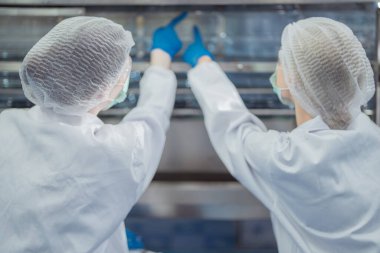 Bilim adamı, endüstriyel fabrikanın makine taşıma hattındaki su şişelerinin kalitesini kontrol ediyor. İçki üretim hattında veri kaydeden kadın işçi..