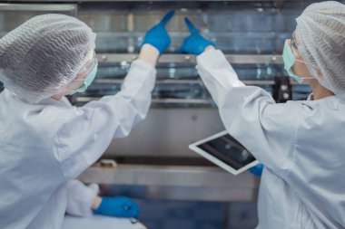 Bilim adamı, endüstriyel fabrikanın makine taşıma hattındaki su şişelerinin kalitesini kontrol ediyor. İçki üretim hattında veri kaydeden kadın işçi..