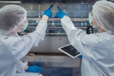 Bilim adamı, endüstriyel fabrikanın makine taşıma hattındaki su şişelerinin kalitesini kontrol ediyor. İçki üretim hattında veri kaydeden kadın işçi..