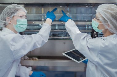 Kadın fabrika işçileri endüstriyel fabrikadaki makine sistemlerini kontrol ediyorlar. Kadınlar içecek ve gıda üretimi için temiz odalarda çalışıyorlar